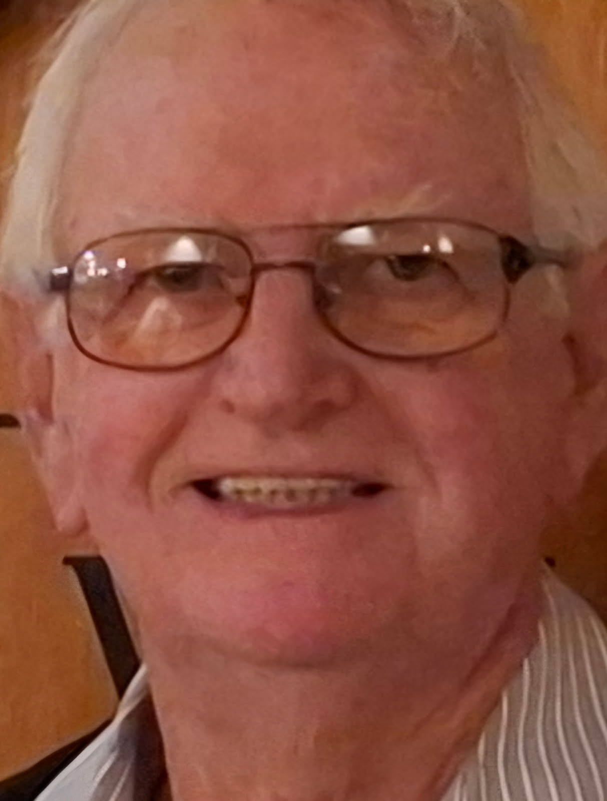 A close-up of Allen smiling, white-haired, in gold-rimmed glasses and a striped shirt.